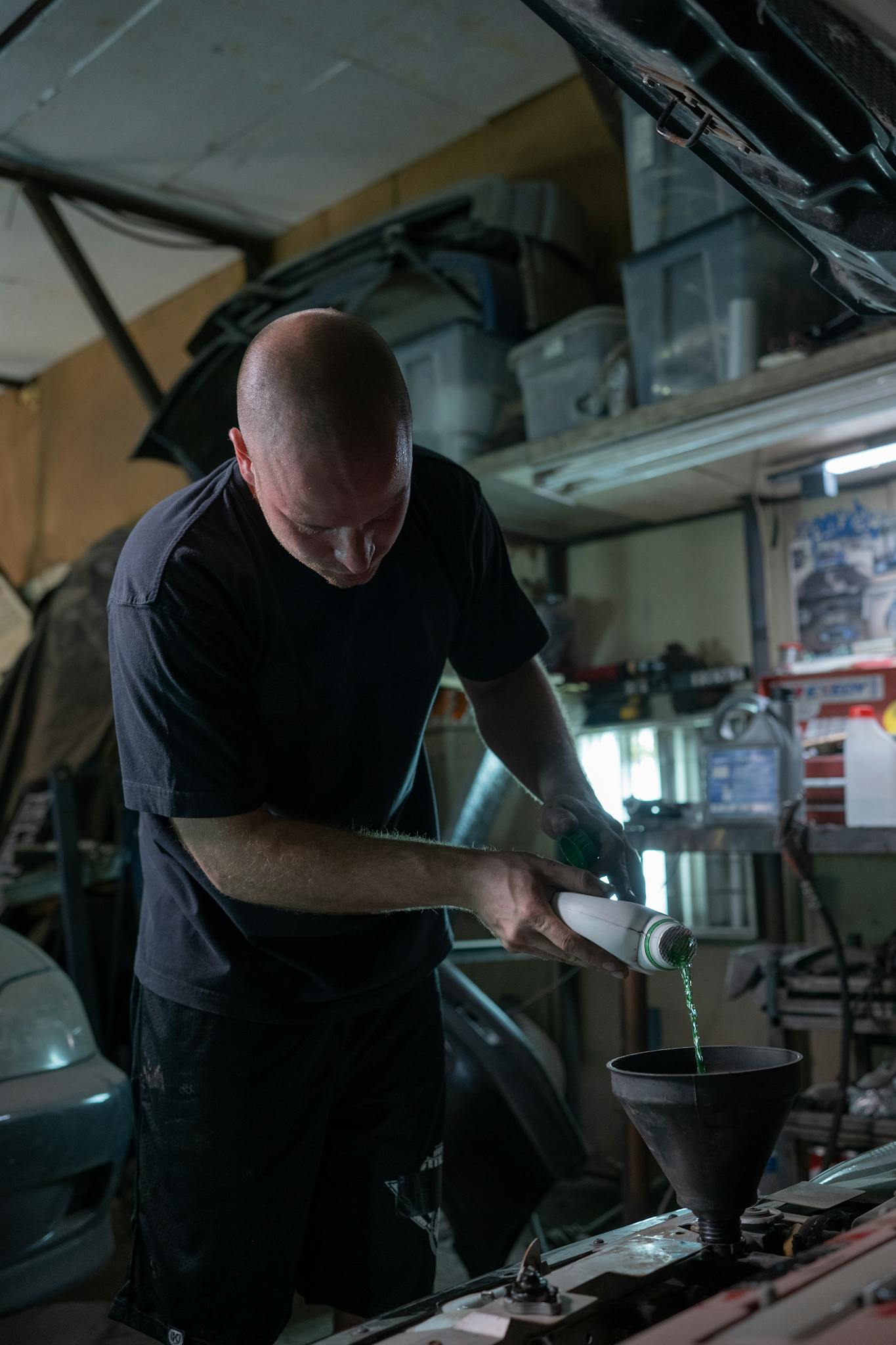 Man pours engine fluid into a vehicle in a dimly lit garage.