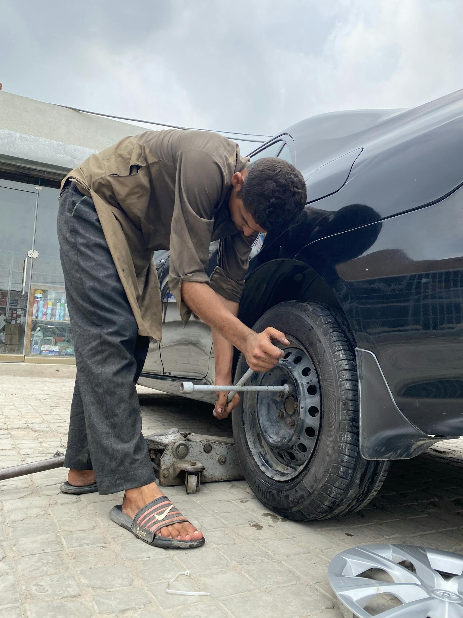 Young man repairing car wheel outdoors, showcasing automotive skills.